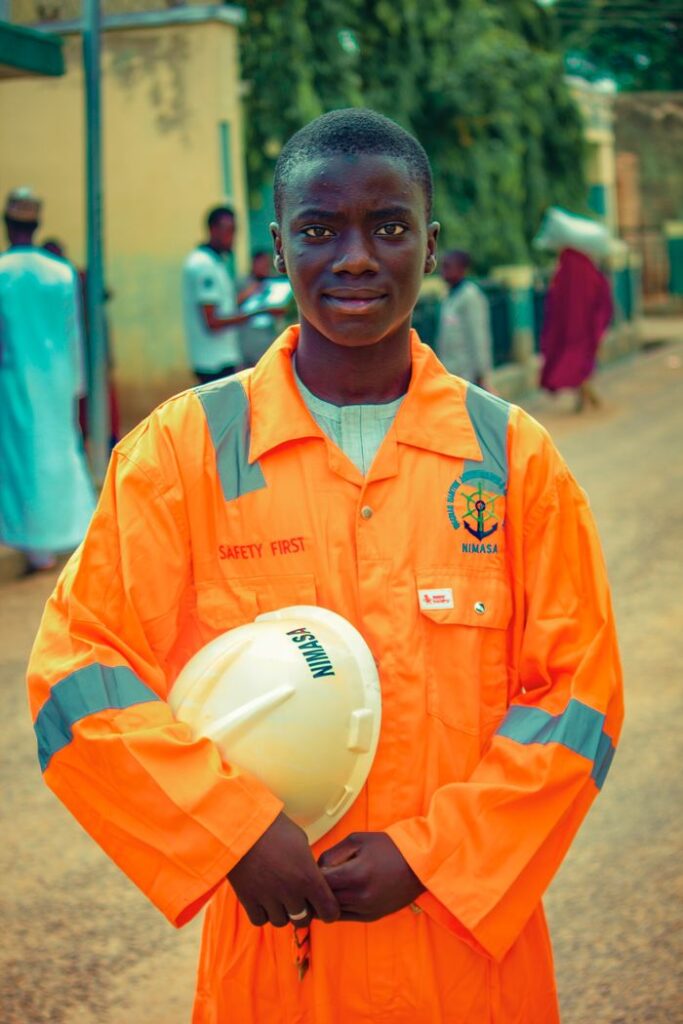 Portrait of a young worker in orange safety gear holding a helmet, standing outdoors.