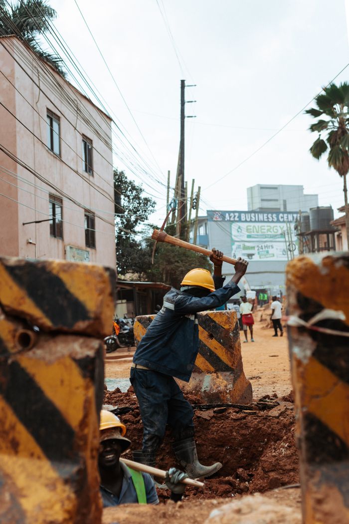 Construction worker with hard hat using a pickaxe in an urban street setting, symbolizing infrastructure development.
