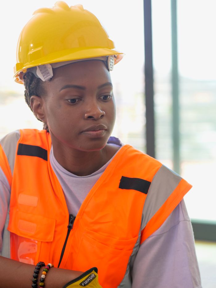 A woman in a hardhat and reflective vest focused on her construction work.